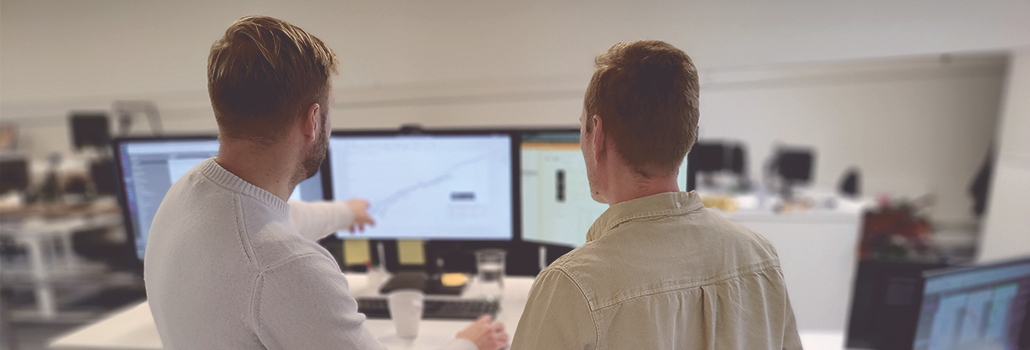 Medarbejdere hos Exigo viser hinanden 5D-økonomistyring for et projekt på en computer
